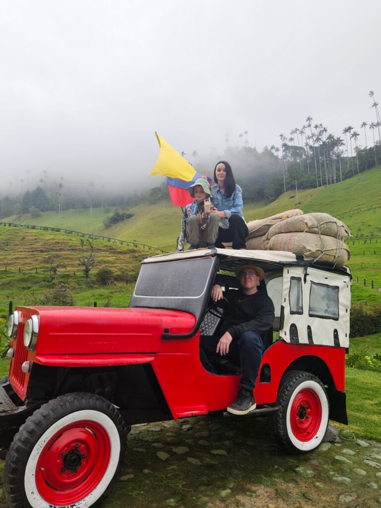 Family riding a vintage red Willys jeep loaded with coffee sacks near wax palms in Colombia's coffee region