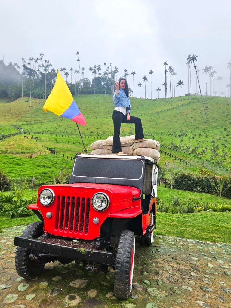 Woman standing on top of a red Willys jeep with wax palms in the background, Cocora Valley