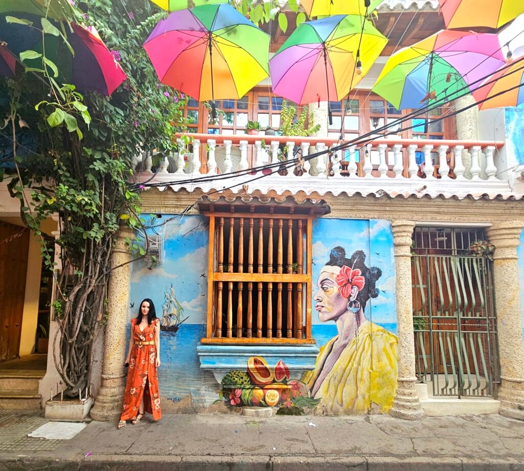 Woman posing beside a colourful mural of a woman and sailing ship in Getsemaní, Cartagena
