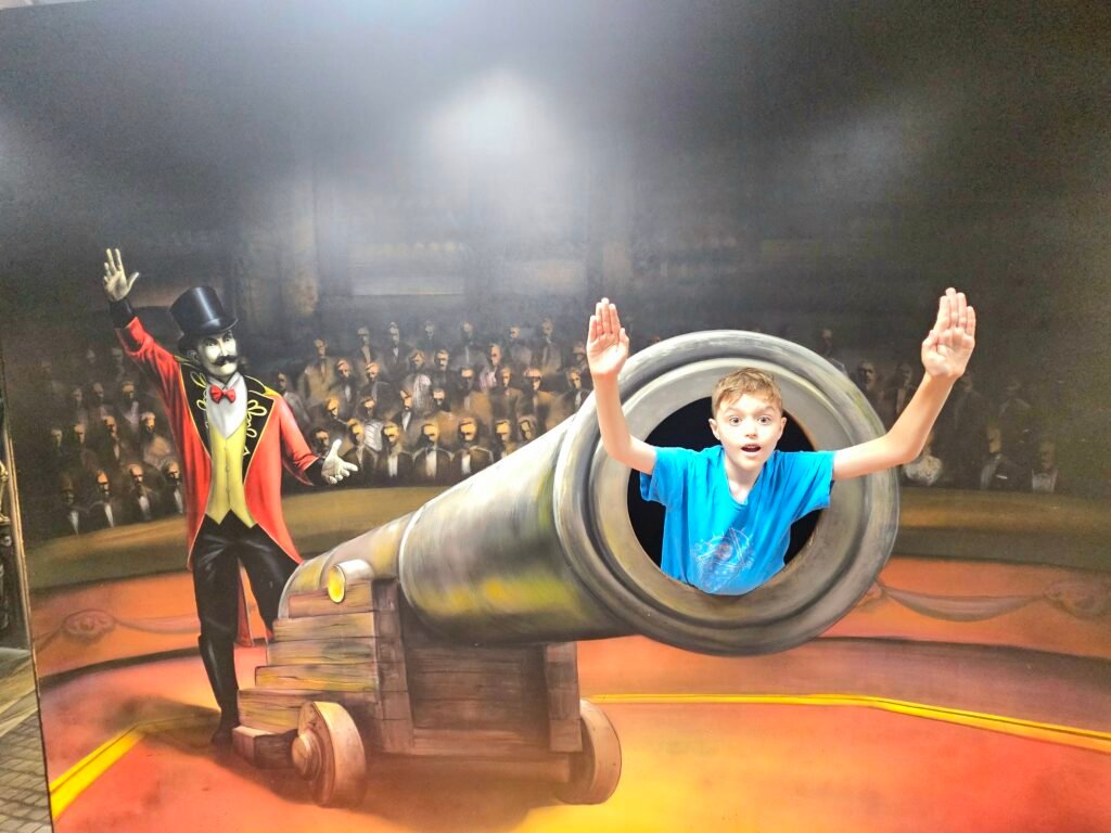 Boy posing inside a 3D circus cannon illusion at the Museum of Fantastic Illusions in Prague