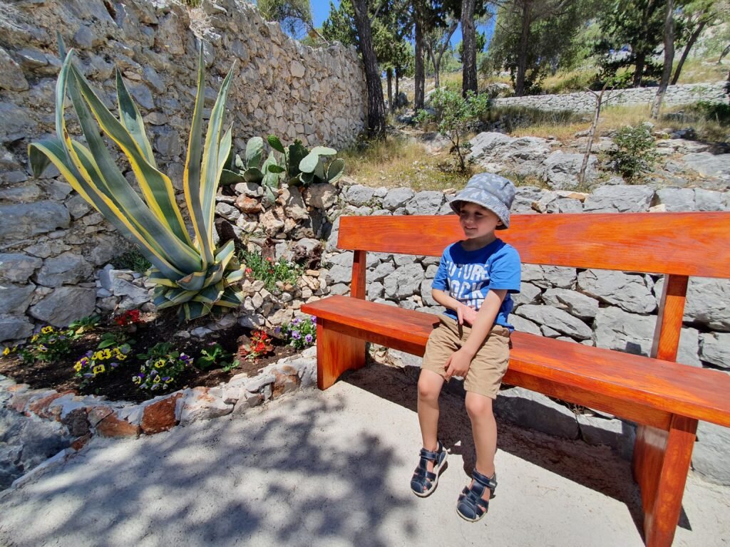 Boy resting on a wooden bench beside a stone wall on Hvar island