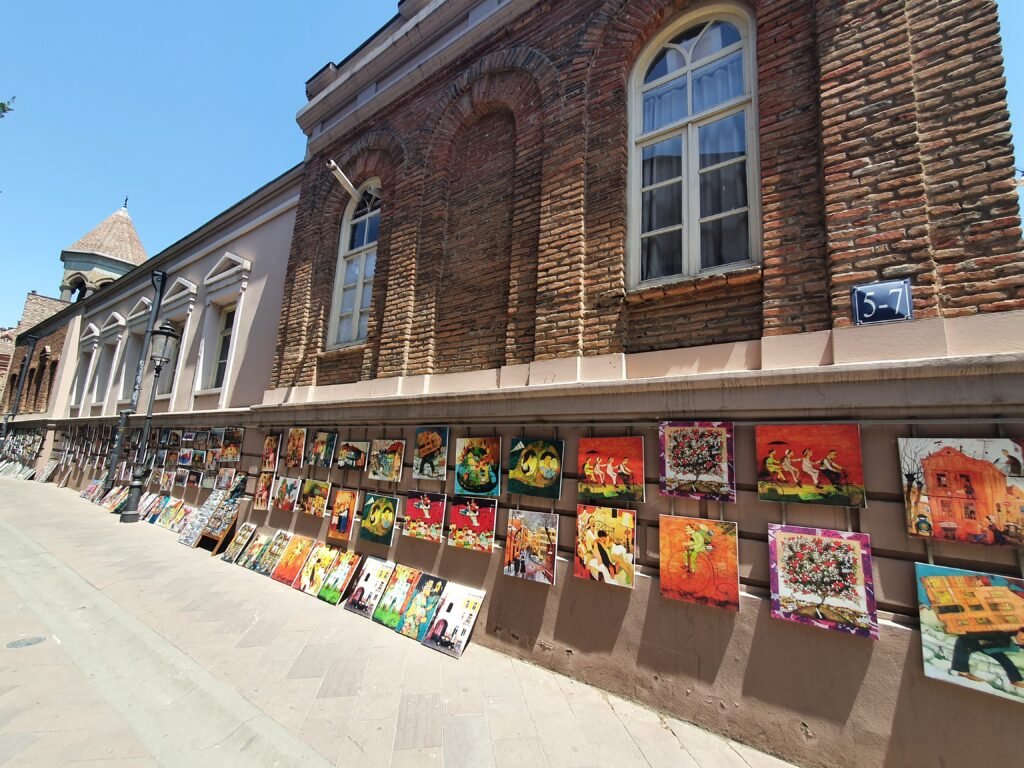 Paintings for sale lined up along an old brick building