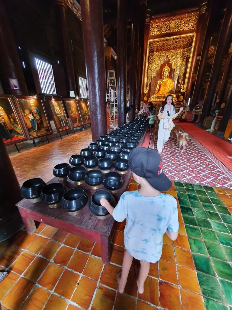 Boy looking at rows of alms bowls inside a Buddhist temple in Thailand