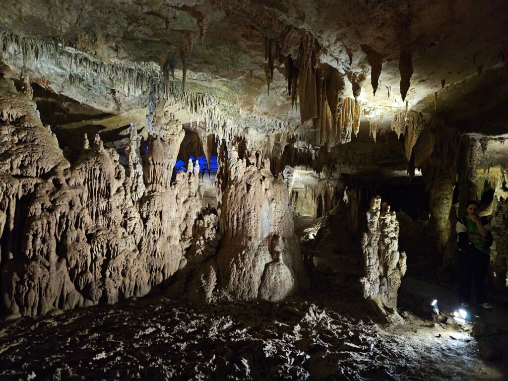 Lit hall inside Prometheus Cave with stalactites and stalagmites along the walking route