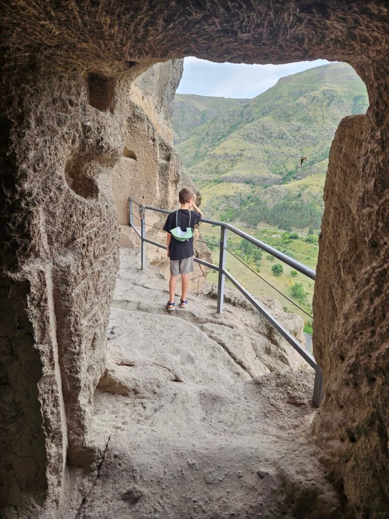 Our son on a railed walkway inside a cave at Vardzia, looking out over the green valley