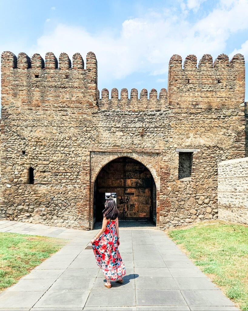 Woman walking towards the gate of an old stone fortress in Georgia